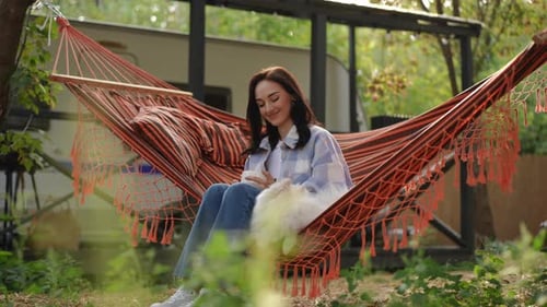 Woman in Hammock with Dog Using Phone
