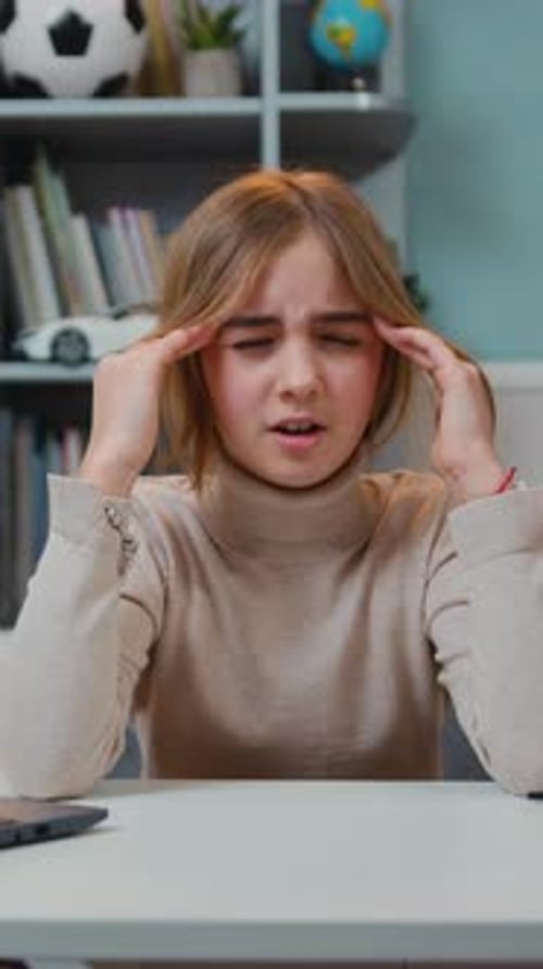 Tired Preteen Girl Sitting By Table with Headache Massaging Her Temples with Circular Motion After a