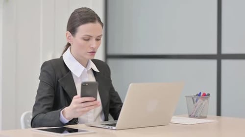Businesswoman Uses Laptop and Smartphone in Office