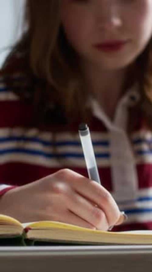 Young Female Student Writing in Notebook at Desk in College