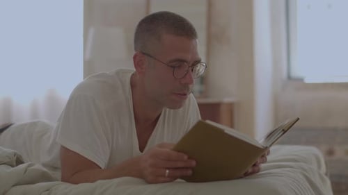 Handsome Man in Eyeglasses Reading Book in Bed in Morning