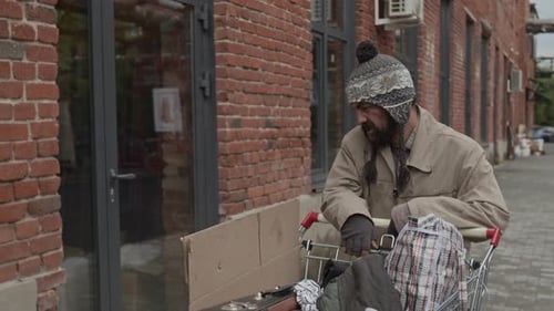 Male Vagrant Pushing Shopping Cart with Belongings Scanning Area for Coins