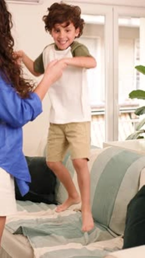 Playful child jumping on sofa with adult indoors