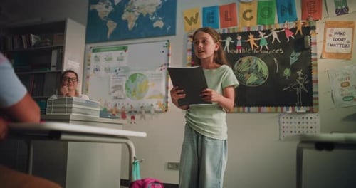Primary School Girl with Notebook Showcasing Knowledge of Ecology in Front of Classmates and Teacher