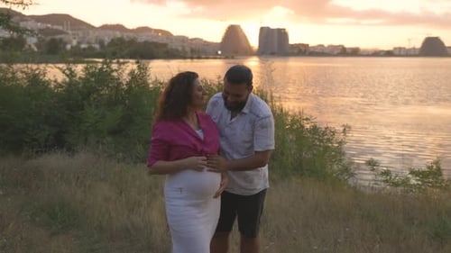 Expectant Couple Posing by Lake at Sunset