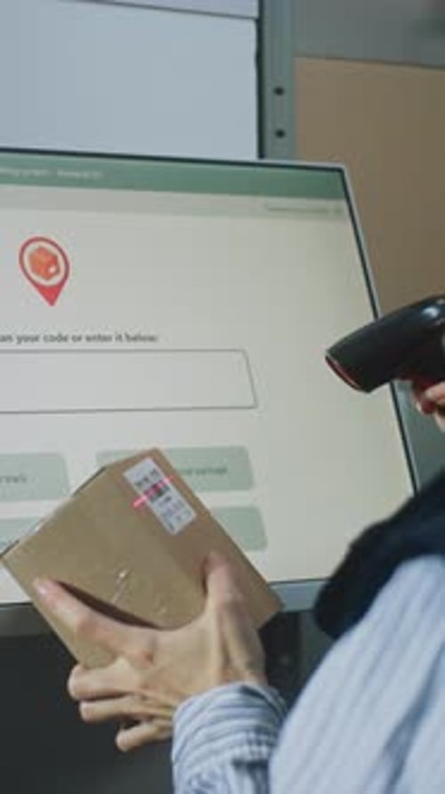 Female Warehouse Employee Scans Cardboard Box at Postal Terminal with Digital Display