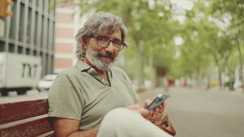 Smiling Man Using Phone While Sitting on Bench