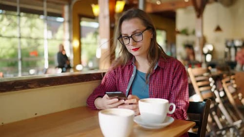 Woman is Using Smartphone and Drinking Coffee in the Cafe