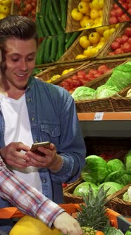 Couple Reviews Their Shopping List on a Smartphone in a Colorful Supermarket