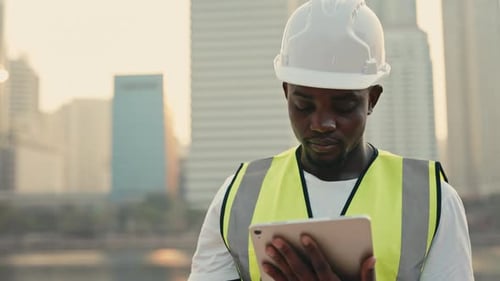 Portrait of African American Engineer Working on Tablet Computer Standing Against Modern Skyscrapers
