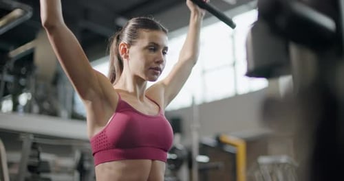 A Young Beautiful Brunette Girl in Sportswear is Exercising on a Machine in the Gym Doing Exercises