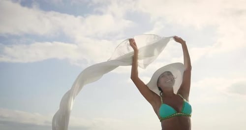 A beautiful young girl strolls along the coast of the sea, in a swimsuit in a straw hat, a white k