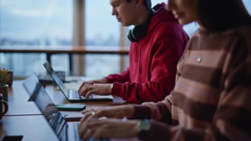 Two Young Adults Working on Laptops in Modern Office