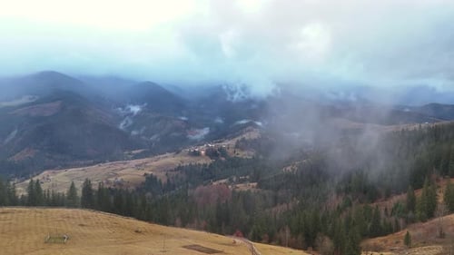 Panoramic View of Misty Mountains and Small Village in Valley Fog Covering Green Pine Forest on