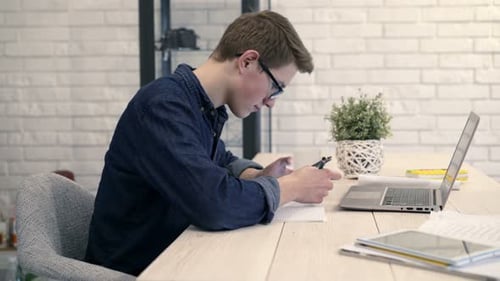 Teenager Using Phone and Writing at Desk Indoors
