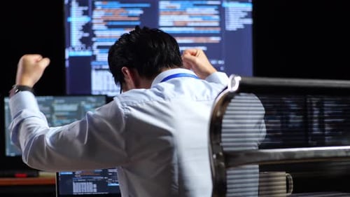 Asiatischer männlicher Programmierer feiert erfolgreiches Schreiben von Code auf einem Laptop mit mehreren Monitoren