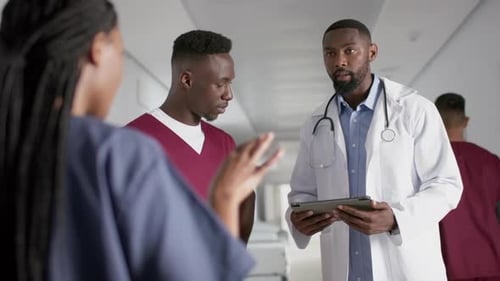 Diverse male and female doctors discussing work, using tablet in corridor at hospital, slow motion