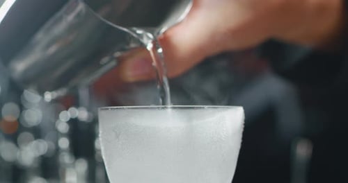 Close up of a professional bartender is preparing an alcoholic cocktail with ice cubes to customer