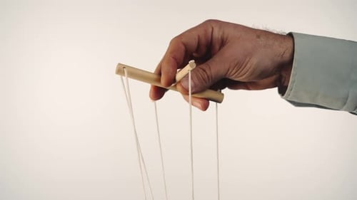 La mano de un hombre con una camisa gris controla una marioneta con un manipulador de madera y cuerdas