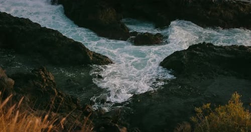 Ocean waves breaking on rocky beach at golden sunset light. Close-up raging stormy sea foam, water s