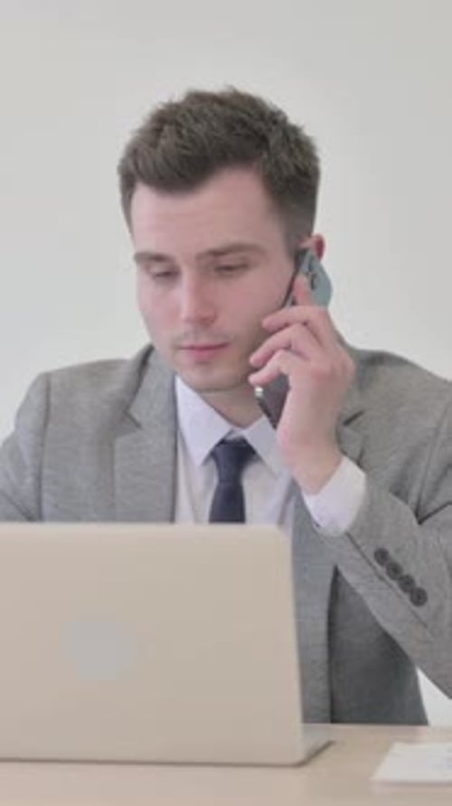 Man in Suit Answers Phone While Using Laptop