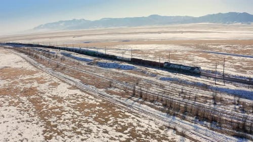 Ein Eisenbahnzug mit Zug und Güterwagen fährt auf der Schiene in der Steppe