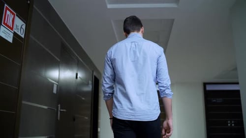 Backside View Young Man Walks Along Hallway in Center