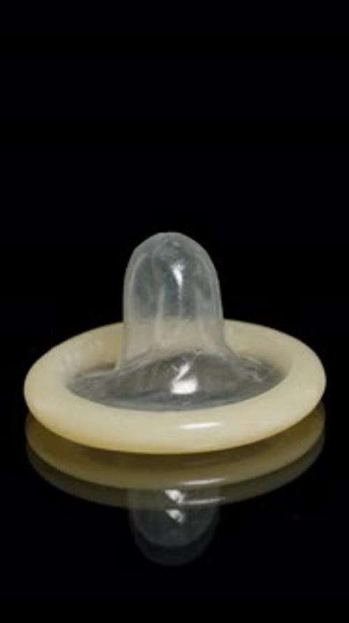 Vertical video. Condom Falling on a Black Reflective Surface Captured in Slow Motion with Close-Up