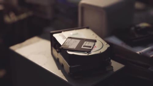 Hard Drive and Floppy Disk Placed on a Dusty Table in a Cluttered Workspace