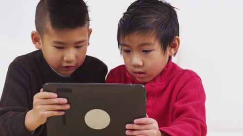 Two cheerful asian boys smiling and touching a digital tablet indoors