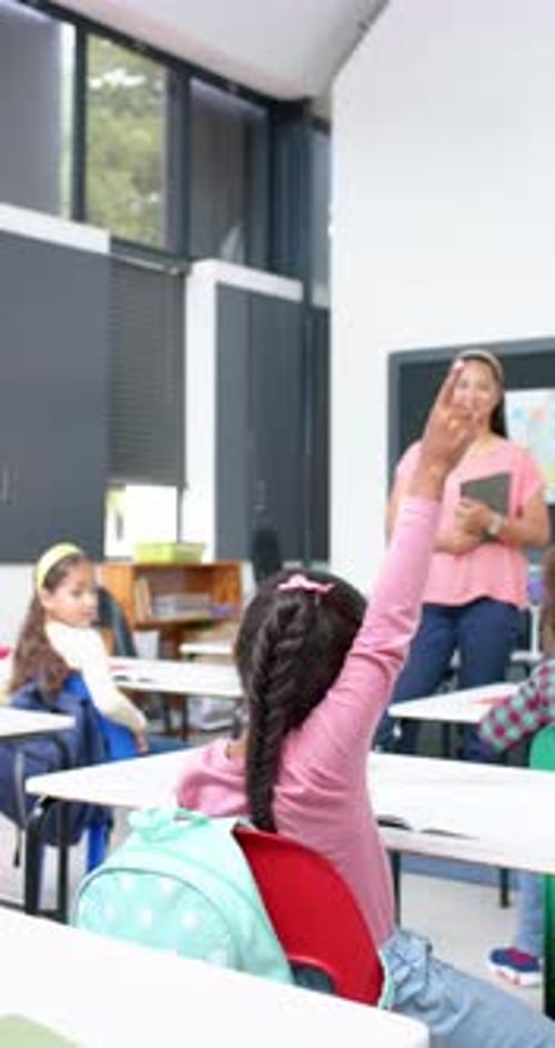 Vertical video: In school, girl raising hand to ask question while teacher smiles