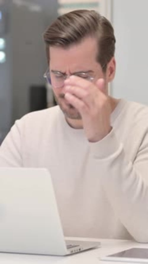 Man Typing on Laptop with Headache in Home