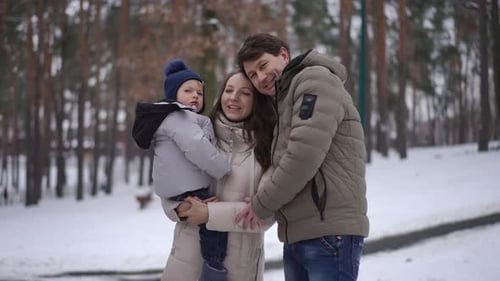Family Smiling and Embracing in a Snowy Park Enjoying a Joyful Winter Moment