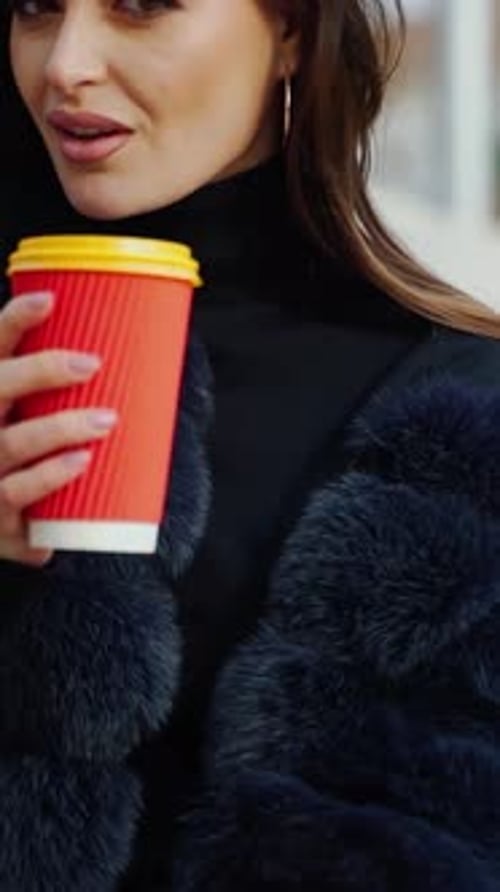 Female hands hold a cup of beverage outdoors.