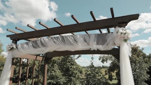 Decorated wedding archway in a outdoor patio garden looking up at a beautiful cloudy blue sky.