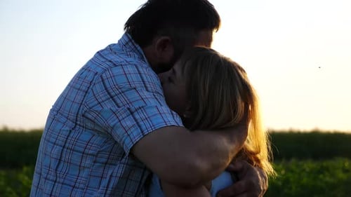 Man and Woman Embrace in Field at Sunset