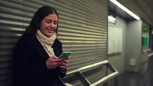 Thoughtful Woman Using Smartphone While Waiting for Transport at Subway Station Engaged in Browsing