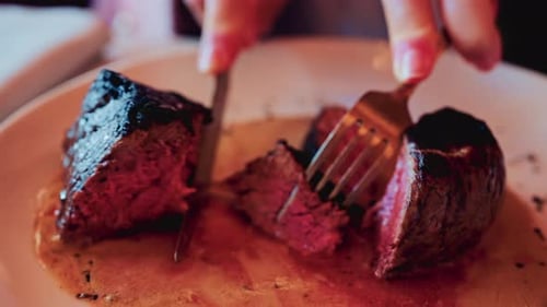 Close up of a knife slicing through a medium rare steak, exposing its tender, juicy interior