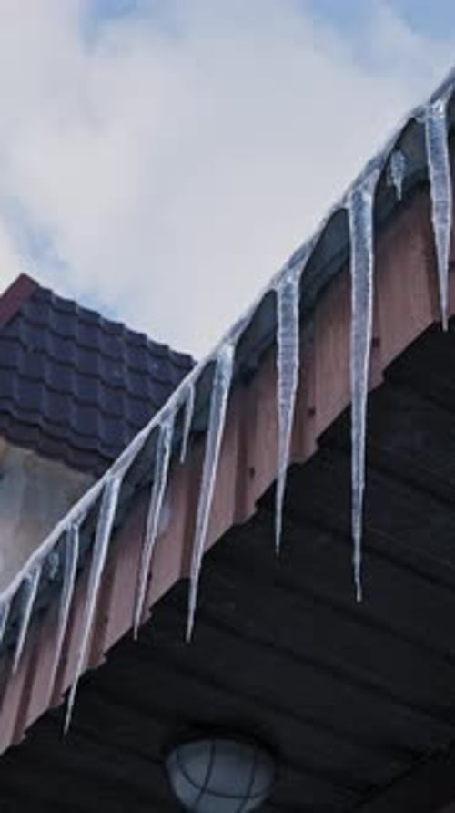 Long Sharp Icicles Hanging From Roof Eaves in Winter