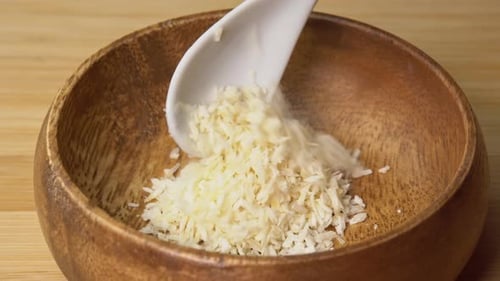 La cuchara coloca las hojuelas de coco en un tazón de madera sobre una tabla de madera y gira. Virutas de coco o ralladas