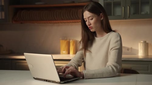 Woman Typing on Laptop in Dark Kitchen at Night