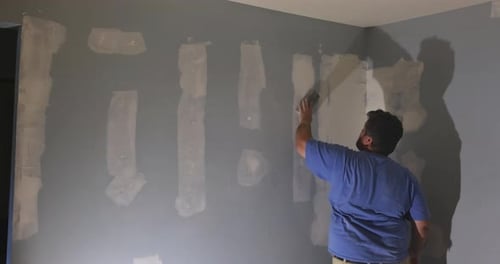 Man Applies Putty to Wall for Painting Project in Home Interior During Renovation Effort
