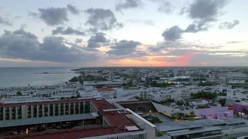 Aerial view of a cityscape by the coast, with built structures, rolling clouds and endless horizon o