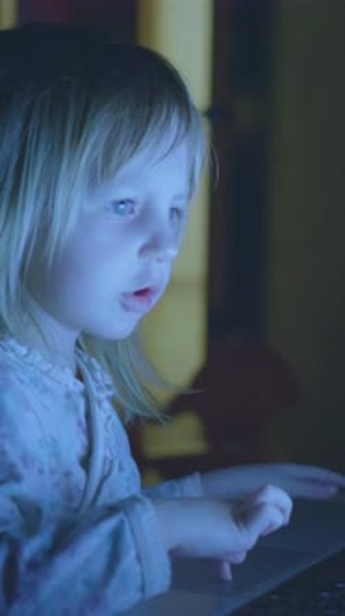 Young Child Focused on Using Laptop in Dimly Lit Room Illuminated By Screen Light Showcasing