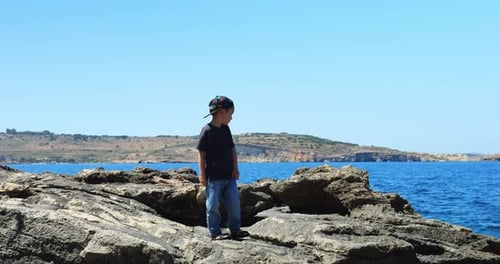 Cheerful Boy Child Confidently Poses on Coastal Rocks Stepping Closer to Edge