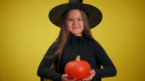 Smiling Girl in Witch Costume Holding Pumpkin