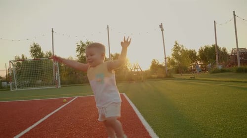 Little boy joyfully runs on a tennis court during sunset in golden light