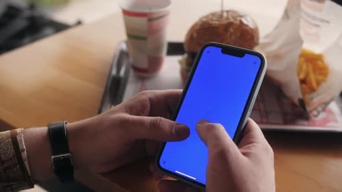Person Sitting at Cafe Using Phone with Blue Mockup Screen Chroma Key Surfing Internet Watching