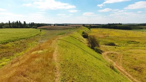 Summer green landscape under blue skies. Long hill separating meadows from agricultural farmlands.