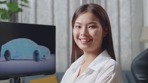Asian Female Designer Crossing Her Arms And Smiling While Working On 3D Model Of Ev Car On Computer